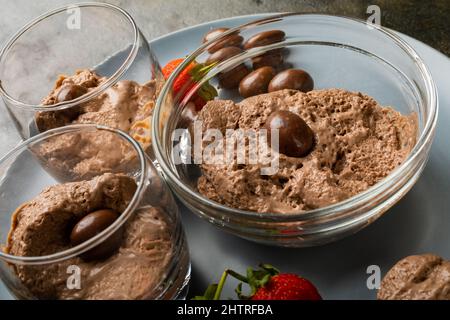 Schokoladenmousse mit überzogenen Nüssen und Erdbeeren in einer Schüssel und Gläsern auf dem Teller serviert Stockfoto