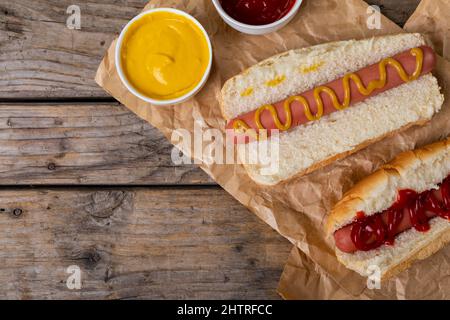 Blick von oben auf Hot Dogs mit Tomaten und mufferten Saucen auf Papiertüten am Tisch Stockfoto