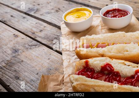 Nahaufnahme von Hot Dogs mit Tomaten und musterten Saucen auf Papiertüten am Tisch Stockfoto