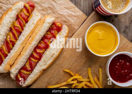 Hot Dogs mit mustert und Tomatensauce serviert mit Getränk und pommes frites am Tisch Stockfoto