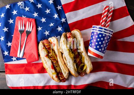 Hot Dogs mit Saucen und Jalapenos serviert auf amerikanischer Flagge mit Gabel, Stroh und Einwegbecher Stockfoto