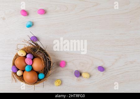 Blick aus der Vogelsicht auf Eier und bunte Süßigkeiten im Nest auf dem Tisch während der osterzeit Stockfoto