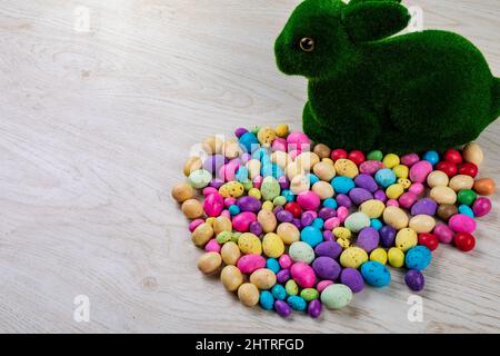 Künstliches Mooshäschen mit bunten Süßigkeiten ostereiern auf dem Tisch mit leerem Platz Stockfoto