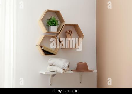Regale mit Pullovern, Hut und Dekor, die an der hellen Wand hängen Stockfoto