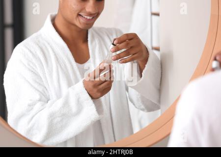 Junger afroamerikanischer Kerl, der Serum für die Hautpflege im Badezimmer verwendet Stockfoto