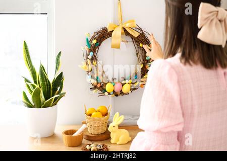 Frau, die einen schönen Osterkranz an der weißen Wand hängend Stockfoto
