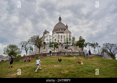 Paris, Frankreich - 2020. April: Während der COVID-19-Sperre spielt ein kleines Mädchen mit ihren Hunden, während sich die Leute auf dem Rasen gerade darin ausruhen Stockfoto