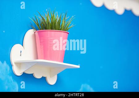 Inneneinrichtung. Rosafarbener Blumentopf mit grüner Pflanze auf weißem Holzregal Stockfoto