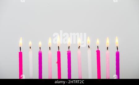 Verschiedene rosa Farbe Geburtstagskerzen brennen in Reihe auf grauem Hintergrund, Studio-Aufnahme, viel Platz für die Kopie für Grüße. Seitenansicht. Stockfoto