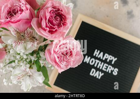 Happy Mother's Day Text auf schwarzem Briefbrett. Rosa Rosen, Gypsophila alstroemeria auf dem Hintergrund. Grußkartenkonzept Stockfoto