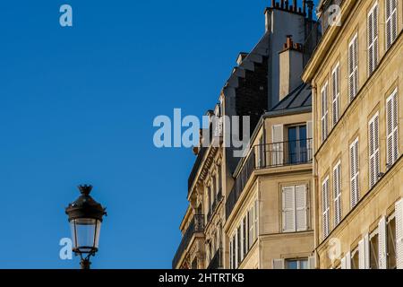 Blick auf eine Laterne und ein typisches Pariser Wohnhaus mit Balkon und Kaminen an einem schönen Tag in Paris Stockfoto