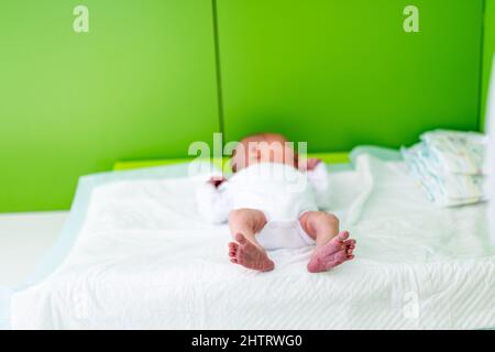 Kleines Baby, das gerade in der Entbindungsklinik geboren wurde, liegt auf dem Wickeltisch im Krankenhauszimmer. Windeln, die im Hintergrund gewechselt werden können Stockfoto