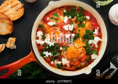 Shakshuka. Hausgemachte Spiegeleier mit Gemüse in eiserner Pfanne auf altem dunklen Schiefer, Stein oder Beton Hintergrund. Traditionelle Küche Israels. Spät Stockfoto