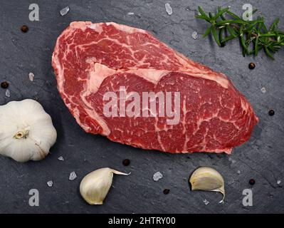 Marmoriertes rohes Fleisch Steak Ribeye auf schwarzem Schieferteller, Draufsicht auf frisches Grillfleisch mit Gewürzen Stockfoto