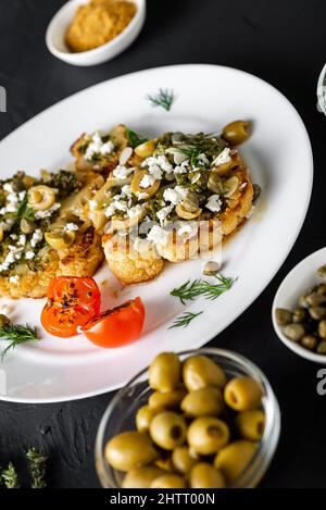 Gebackenes Blumenkohlsteak mit Chimichurri-Sauce, Mandelflocken, Kapern. Vegetarische Gerichte. Alternative leckere Speisen. Stockfoto