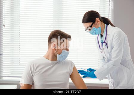 Der Arzt hält eine Spritze in der Hand, bevor er einem Patienten eine Injektion in einer medizinischen Maske verabreicht. Covid-19- oder Coronavirus-Impfstoff. Impfung der Bevölkerung Stockfoto
