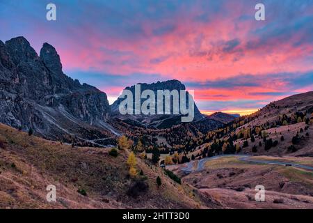 Colorfol Sonnenuntergang über der Sellagruppe (links) und der Langkofelgruppe in der Ferne, eine kurvenreiche Straße, die zum Grödner Pass führt. Stockfoto