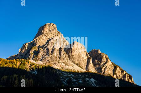 Mountain Mt. Sassongher, Sass Songher, ragen über der Stadt und bunte Bäume im Herbst. Stockfoto