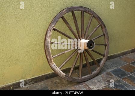 Veraltetes Vintage-Holzrad auf verblichenem gelben Wandhintergrund Stockfoto