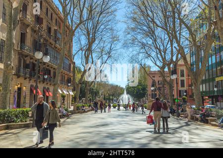 Unbekannte Touristen und Einheimische gehen an einem sonnigen Tag eine Fußgängerzone in Palma Mallorca entlang. Geschäfte, Bäume säumen die Straße mit einem Brunnen am fa Stockfoto