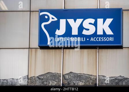 Locarno, Schweiz - 29. Dezember 2021: Ein Schild für den Möbelgiganten Jysk an der Glasfassade mit Bergen unter dem Schild als Spiegelung im Wal Stockfoto