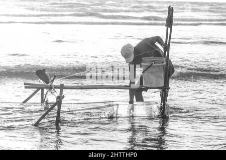 Schwarz-Weiß-Aufnahme eines Fischers, der Fische im Wasser fängt Stockfoto