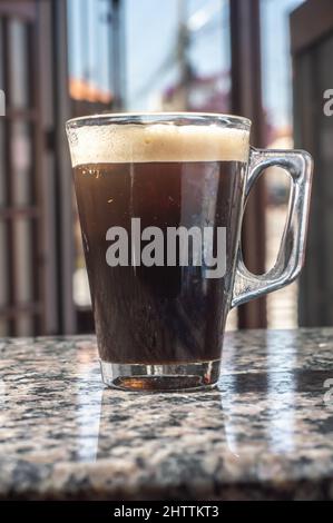 Tonic Kaffee in einer transparenten Tasse, die auf einem marmore-Tisch ist, Stadtklima im Hintergrund. Stockfoto