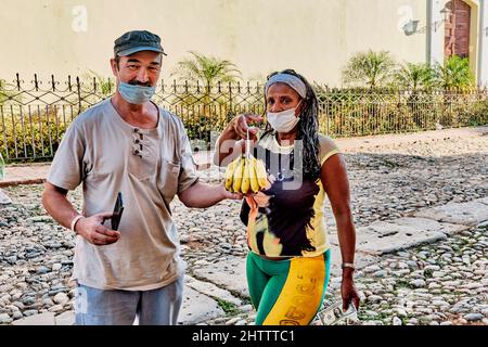 Erwachsene asiatische männliche Touristen kaufen frische Bananen von lokalen schwarzen Frau auf der Straße in Trinidad, Kuba Stockfoto