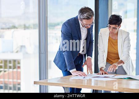 Entwicklung neuer Strategien. Aufnahme von zwei Kollegen, die gemeinsam in einem Büro über Papierkram gehen. Stockfoto