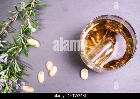Nahaufnahme eines Glases Whiskey mit Walnüssen und einer Rosmarinblume auf einem Steintablett Stockfoto