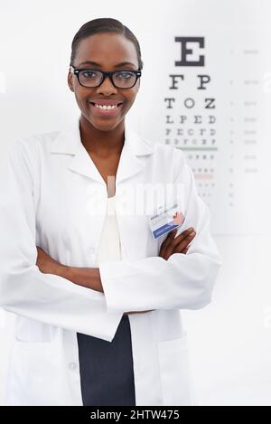 Wie klar können Sie sehen. Porträt einer weiblichen Optometristin, die neben einer Augentestkarte steht. Stockfoto