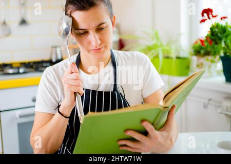 Frau hält Kochbuch und denkt über Idee Abendessen in der Küche. Stockfoto