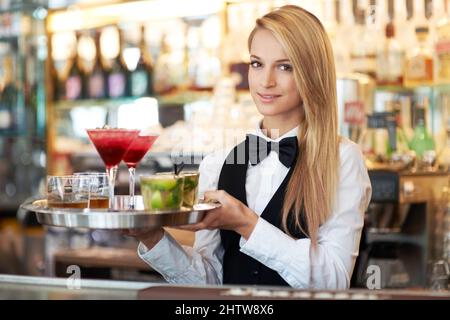 Cocktails für zwei Personen. Attraktive junge Frau, die als Barkeeperin arbeitet und ein Tablett mit Cocktails hält. Stockfoto