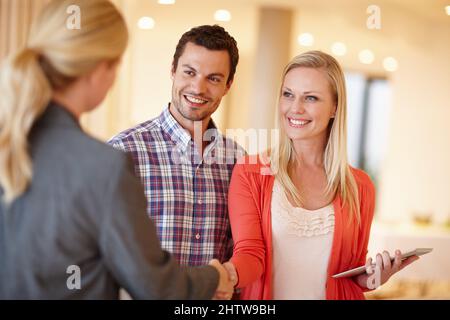 Finanzielle Beratung, der Sie vertrauen können. Ein glückliches Paar schüttelt sich die Hände mit ihrem Finanzberater bei sich zu Hause. Stockfoto