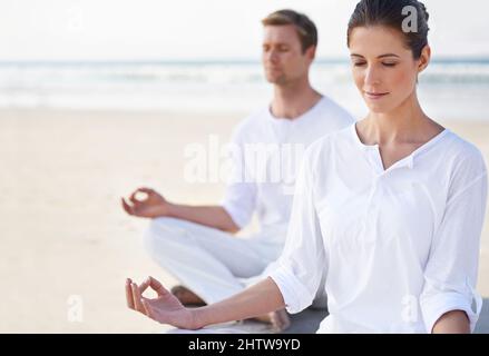 Yoga am Meer. Ein junges Paar, das am Strand Yoga praktiziert. Stockfoto