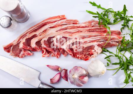 Rohe Lammkoteletts auf dem Küchentisch mit Knoblauch, Rucola, Gewürzen Stockfoto