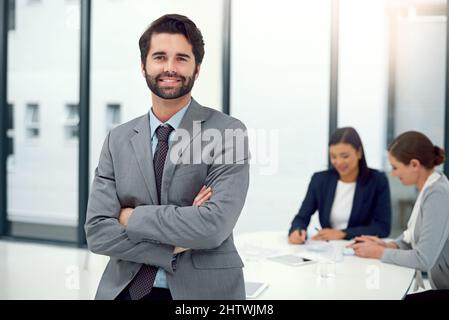 HES führt den Weg nach vorn. Porträt eines Geschäftsmannes, der in einem Sitzungssaal mit Kollegen im Hintergrund steht. Stockfoto