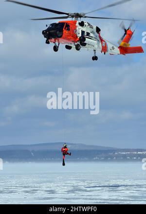 Der Petty Officer der Klasse 3., James Lowen, ein Rettungsschwimmer der Air Station Traverse City, wird am 26. Februar 2022 während einer massiven Eisrettungsübung in der städtischen Marina von Petoskey auf das Eis gesenkt. Die Übung, bei der der Absturz eines Pendlerflugzeugs auf dem gefrorenen Lake Michigan simuliert wurde, brachte mehr als 100 Ersthelfer und Mitglieder der Küstenwache aus dem gesamten Norden von Michigan zusammen. Foto der US-Küstenwache vom Chief Petty Officer John Masson. Stockfoto