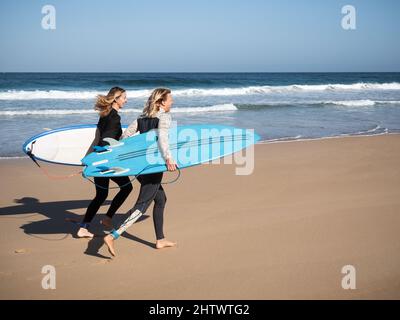 2 Surferinnen laufen mit Surfbrettern am Strand Stockfoto