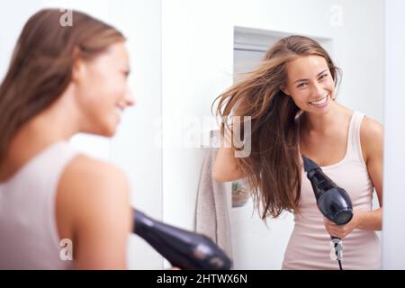 Kümmert sich um ihre üppige Mähne. Eine junge Frau föhnt ihr Haar vor einen Spiegel. Stockfoto