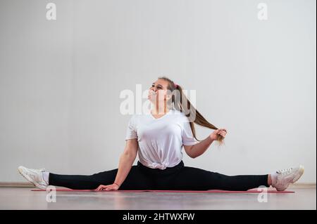 Mollige junge Frau macht Dehnung auf weißem Hintergrund. Stockfoto