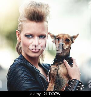 Hes ist ein Rockstar. Beschnittenes Porträt einer kantigen jungen Frau, die ihren kleinen Hund im Freien hält. Stockfoto