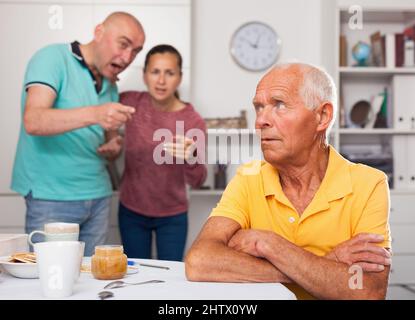 Verärgert älterer Mann am Tisch sitzend, Familienpaar streitend Stockfoto