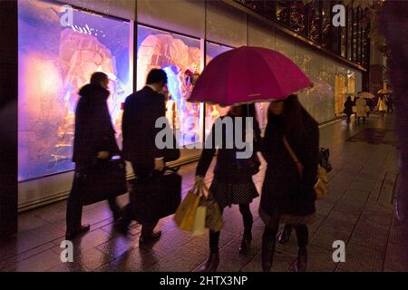 Fußgänger kommen in Ginza, Tokio, Japan unter einem Schirm vorbei Stockfoto