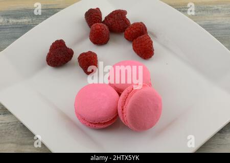 Himbeer-Makronen mit frischen Himbeeren auf weißem Dessertteller auf dem Tisch Stockfoto