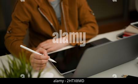 Freiberufliche Mitarbeiterin, die an ihrem tragbaren Tablet-Touchpad und ihrem Laptop-Computer im Co-Working-Bereich arbeitet. Stockfoto