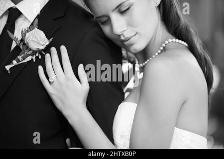 Träumen in Schwarz und Weiß. Schwarz-weißes Bild einer schönen Braut, die ihren Mann von hinten liebevoll umarmt. Stockfoto