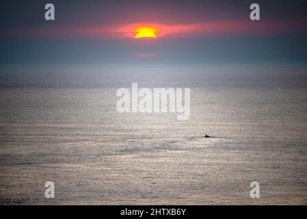 Mit Blick nach Westen zur untergehenden Sonne, über den ruhigen und friedlichen Atlantischen Ozean, an einem ruhigen, ruhigen Sommerabend, hält sich ein entfernter Felsengipfel auf Stockfoto