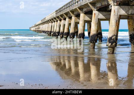 Lange, sich wiederholende Strukturmuster, Reflexion im nassen Sand und abnehmende Perspektive und Schatten der Struktur unter Tolaga Bay Wharf, Ostküste N Stockfoto