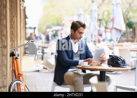 Sein erster Halt am Morgen Aufnahme eines jungen Geschäftsmannes, der mit einem digitalen Tablet in einem Café im Freien sitzt. Stockfoto